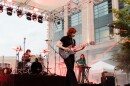 A woman in black playing electric guitar on an outdoor stage
