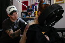 A person lays face down in a massage chair as another person tattoos their back
