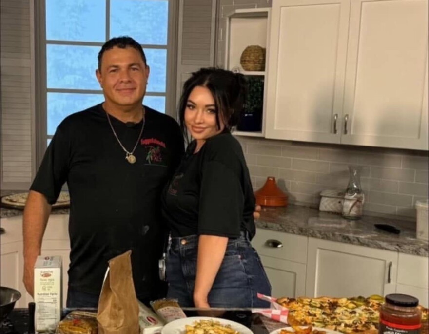 Frank and Alyssa Cappello are posing for a photo in front of a kitchen table. 