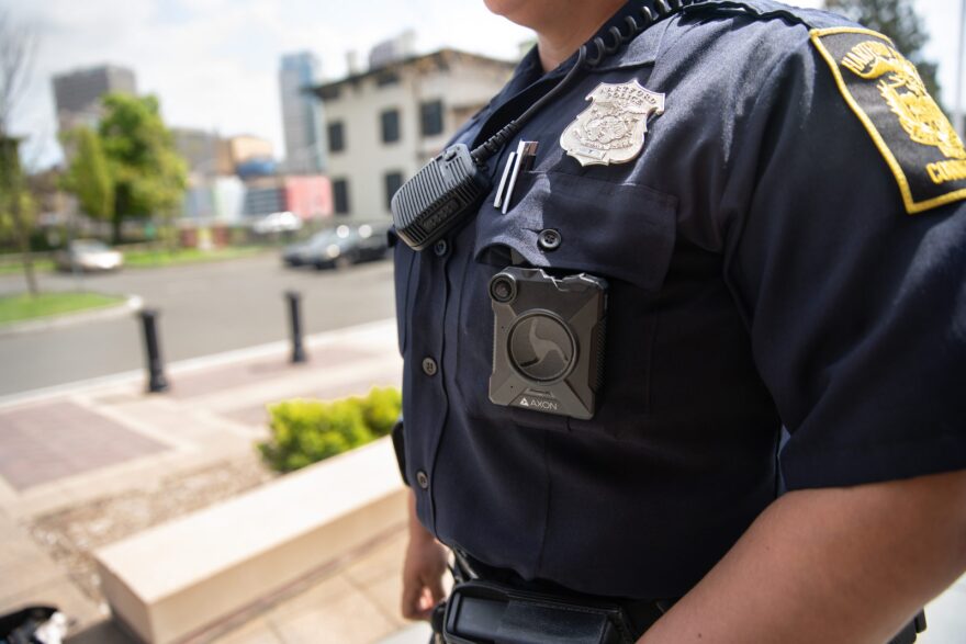 Police officer wearing a uniform with a body camera and radio, emphasizing technology in law enforcement for public safety and DUI checkpoint documentation.