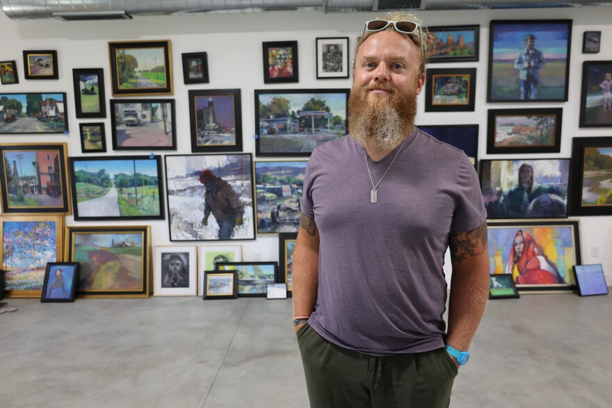 Painter Wyatt LeGrand Poses in front of a wall covered in his piantings.