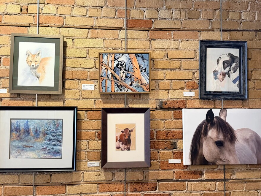 Six framed works of art (all of animals) hanging on a brick wall