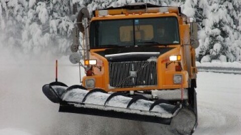 A snow plow clears a road with snow covered tree in the background.