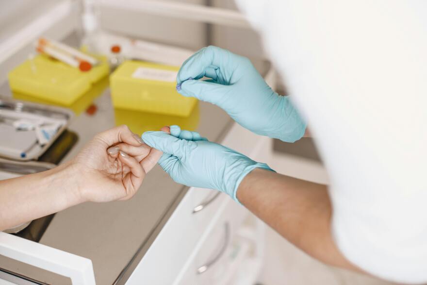 A nurse taking a blood sample from a finger.