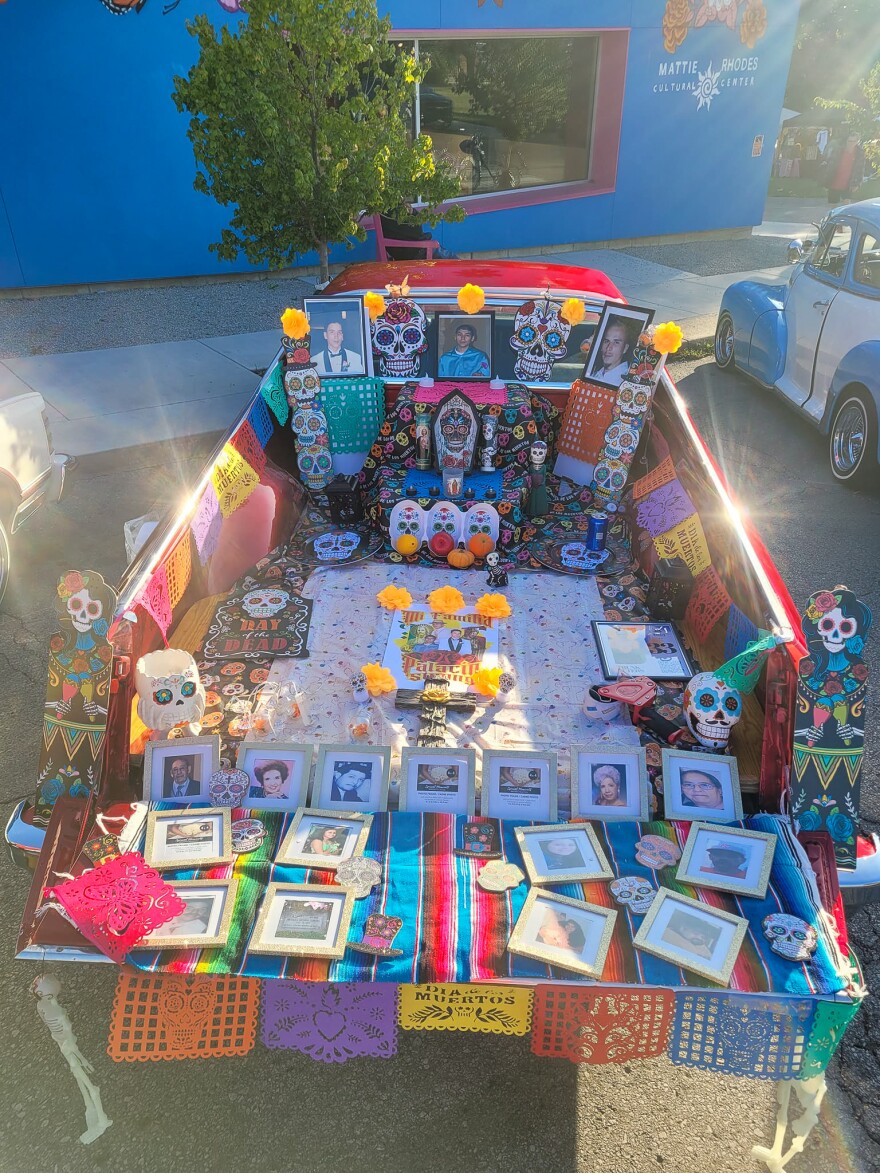 The bed of a ruby red 1973 El Camino is decorate with colorful flags, skull prints and photos of people.