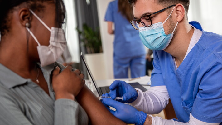Male nurse with mask giving vaccine to patient in clinic.