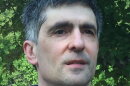A man with short grey hair, wearing a blue polo shirt