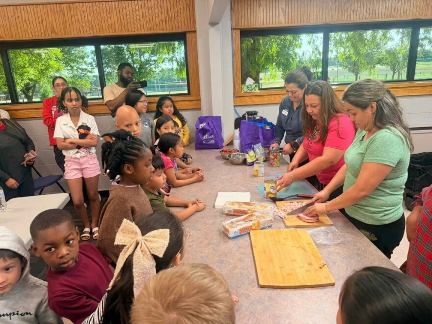 Adriana Figueroa, of K-State Extension, far right, with the can opener, teaches Dodge City Public Schools’ students and their families how to make healthy, family-friendly meals during an evening district-wide event.