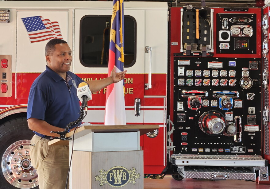 A man gestures to a fire truck while standing at a lecturn.