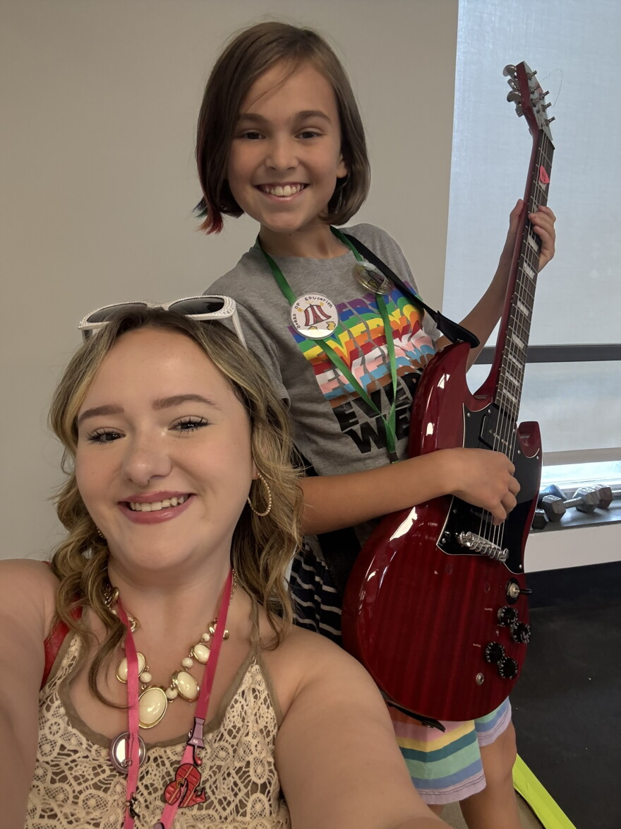 A selfie of two smiling people, with one holding a red electric guitar.