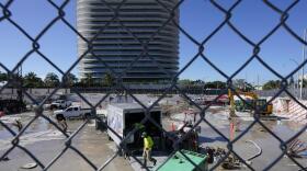 Workers pump water out of the foundation of the former Champlain Towers South building, Thursday, May 12, 2022, in Surfside, Fla. The Eighty Seven Park building is to the south. Parties associated with the building and others have agreed to a settlement of $997 million to compensate the victims and families of those killed when the Champlain Towers South building collapsed nearly a year ago. (AP Photo/Marta Lavandier)
