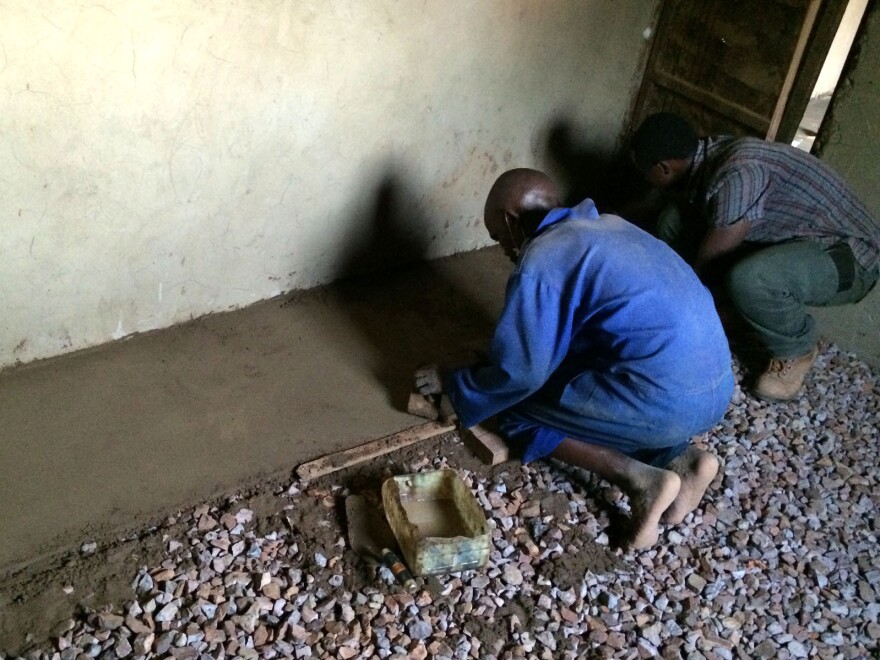 Gravel helps keep the floor level and prevents moisture from seeping up. The floor installers are Jean Pierre (left), a mason, and Daniel Shenyi, operations manager for EarthEnable.
