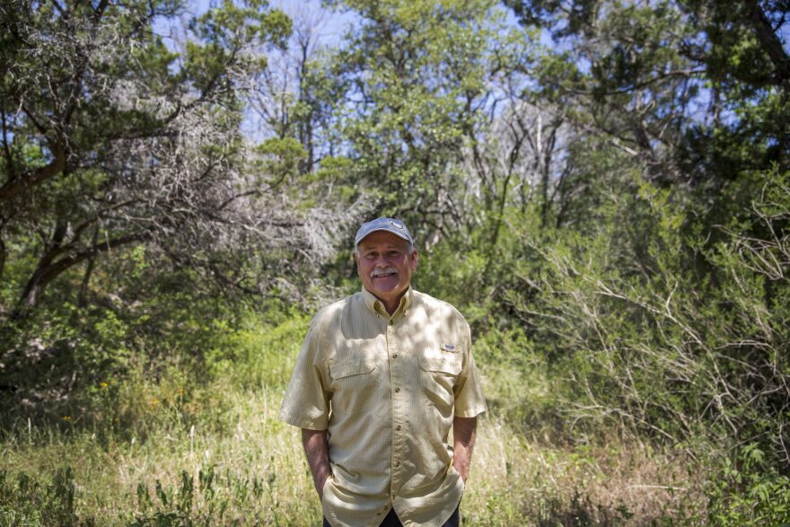 A man standing in the middle of a wooded area with grass and trees surrounding him. 