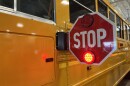 The side of a yellow school bus with a red stop sign extended.  Visible behind the stop sign is a housing for cameras that are intended to catch drivers illegally passing the bus.