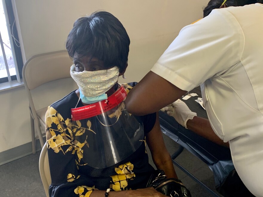 Health worker vaccinates Lolita Johnson, who is wearing a black and yellow dress, as she sits in a chair.