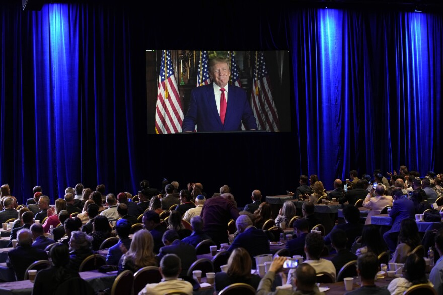 FILE - People listen as former President Donald Trump speaks remotely to an annual leadership meeting of the Republican Jewish Coalition Nov. 19, 2022, in Las Vegas. Trump has spent years teasing the prospect of another presidential run. But in the first week since announcing his third bid for the White House, he's done little to suggest that he's organizing a traditional campaign. (AP Photo/John Locher, File)