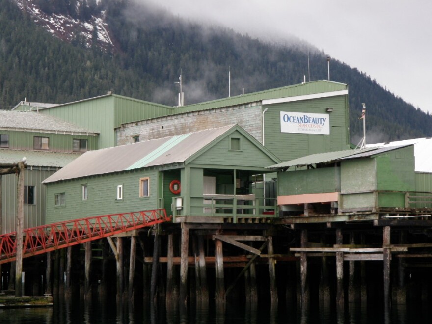 A light green building on piling with a mountainous backdrop.