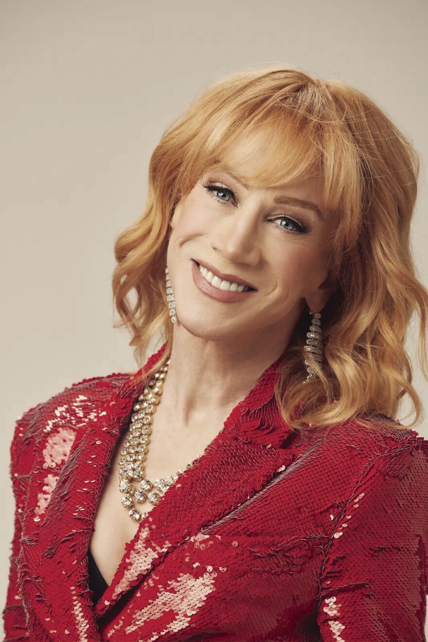 Woman with red hair, wearing red dress, smiles at camera.