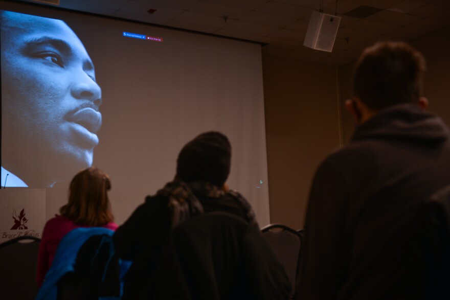 Three people sit in the foreground silhouetted against a large projection screen where the closeup face of Martin Luther King Jr. is projected.