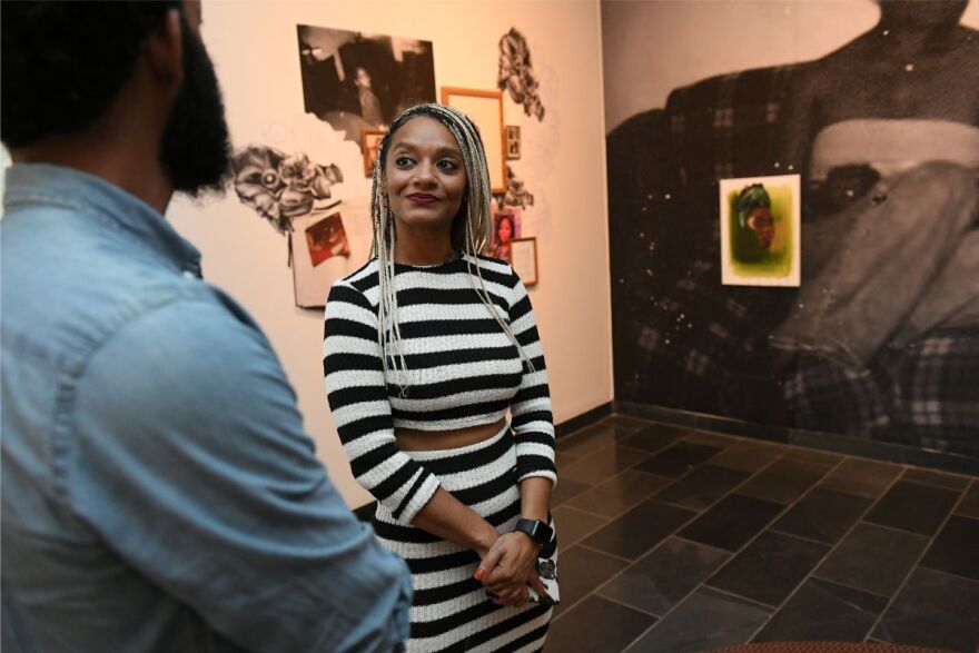 Tatyana Fazlalizadeh stands in front of her gallery installation. She speaks with a man in the foreground who has his back turned to the camera.