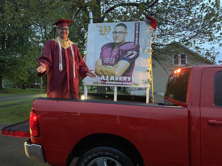 Ali Avery Jr., who goes by A.J., stands in the back of his family's pickup truck in the driveway of his home. His family decorated their vehicle for the drive-through ceremony.