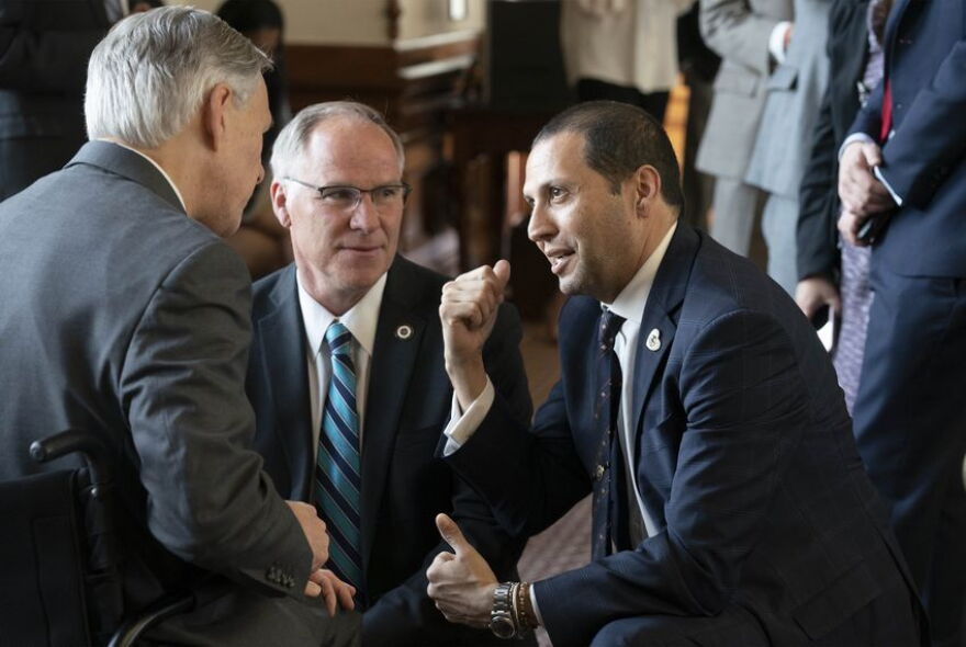 Gov. Greg Abbott talks with state Reps. Kyle Biedermann, R-Fredricksburg (left) and Poncho Nevarez, D-Eagle Pass, on the House floor in March.