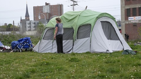 A woman stands near her tent at a nhomeless encampment before city workers arrived to clean up the area, Tuesday, May 16, 2023, in Portland, Maine.