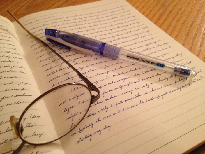 Glasses and a pen sit on a notebook.