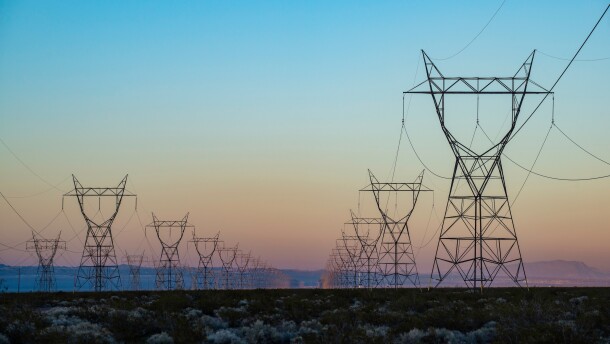 The silhouette of a power transmission line vanishing into a point in the distance during sunset.