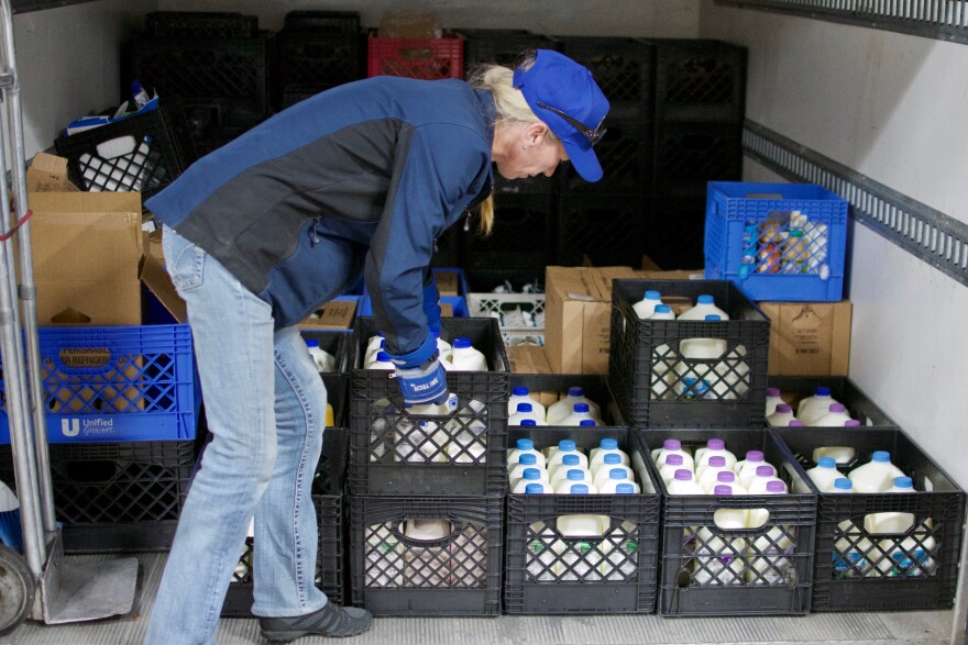 Woman wearing jeans, a jacket and pants unloading a truck full of milk crates.