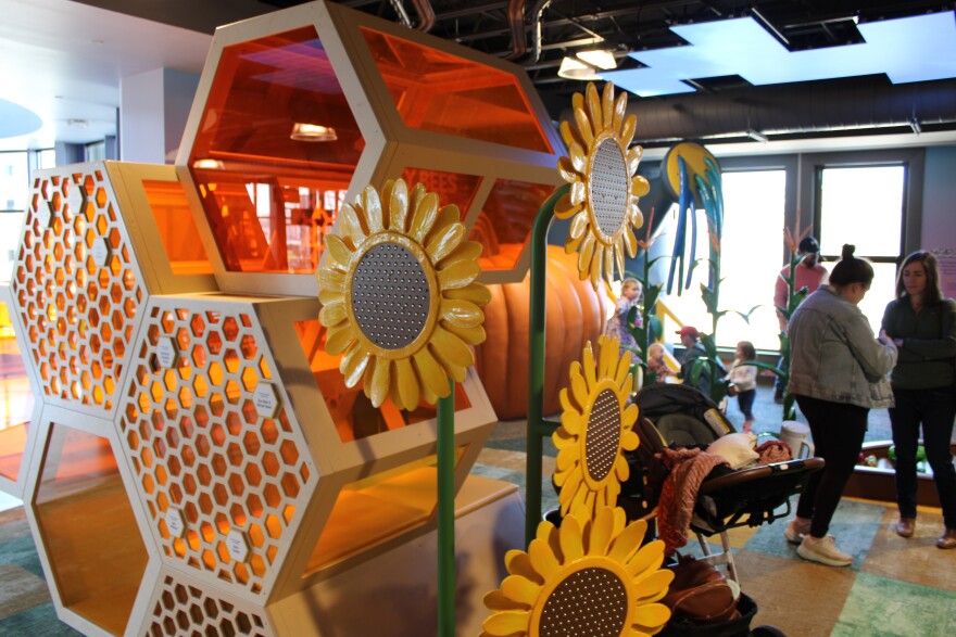 A giant honeycomb structure stands inside a room, with kids playing behind and parents standing. 