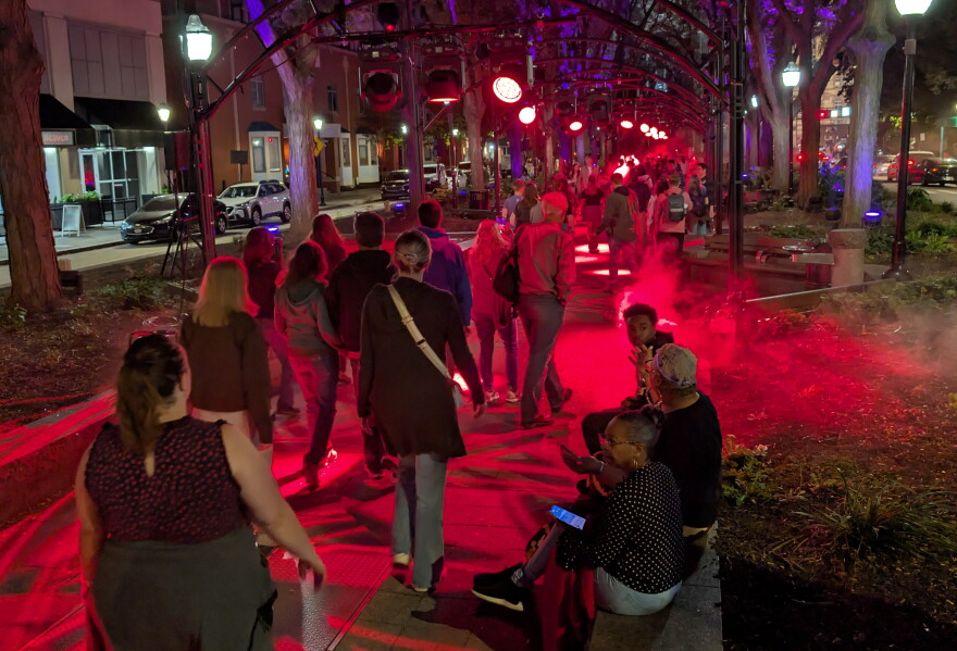 People walk through a narrow park, bathed in red light.