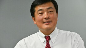 A man wearing a white shirt and red-striped tie sits looking at the camera.