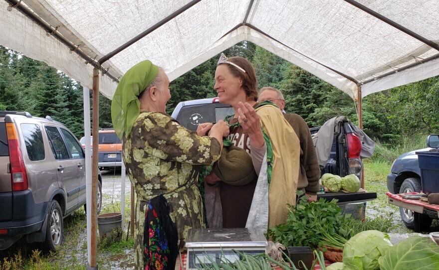 a woman puts a crown and cape on another woman, under a tent