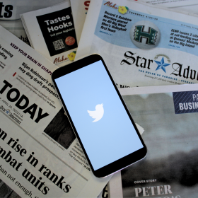 Local and national newspapers with a phone in the center with the Twitter, X, logo