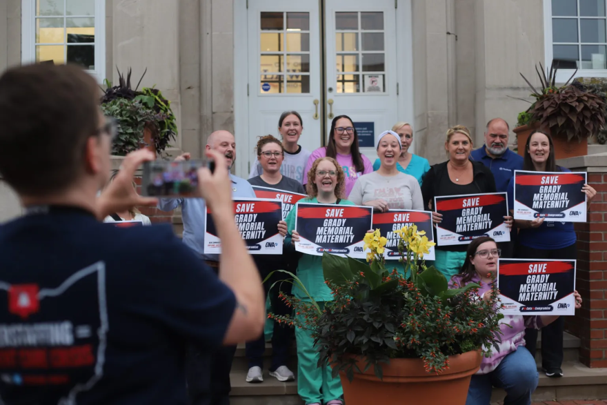A group of health care workers stand together holding signs that say, "Save Grady Memorial Maternity."