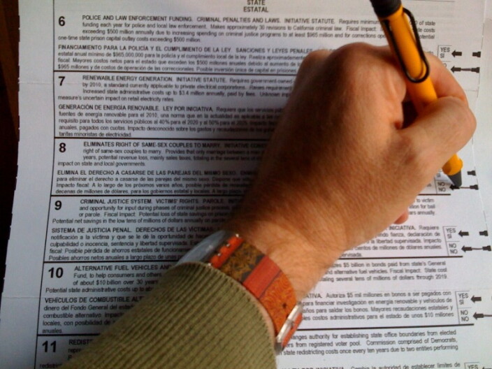 A hand holding a pen filling out a voting ballot.
