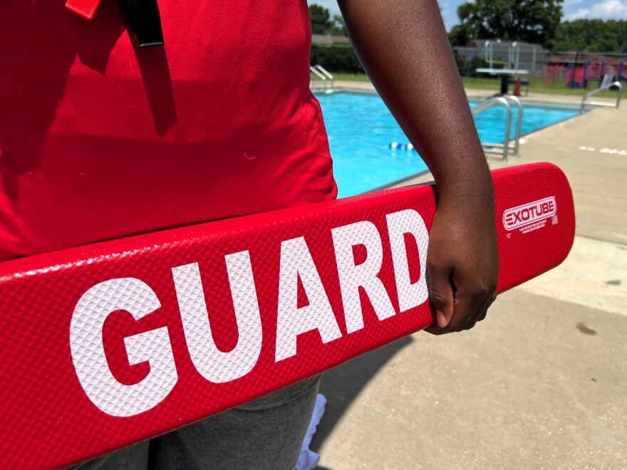 A lifeguard in a red shirt holds a red flotation device.