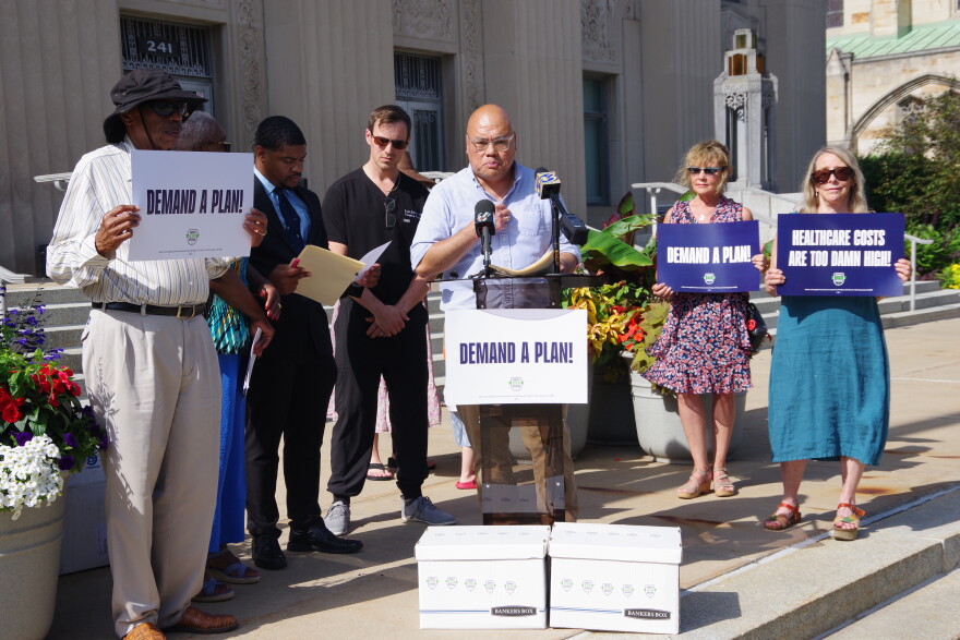City Action and Kalamazoo Forward spokesperson Azlan Ibrahim speaks at a press conference on the steps of Kalamazoo City Hall on July 1, 2026, announcing the submission of signatures to the Kalamazoo City Clerk to put a Healthcare Action Plan on the city of Kalamazoo November ballot.