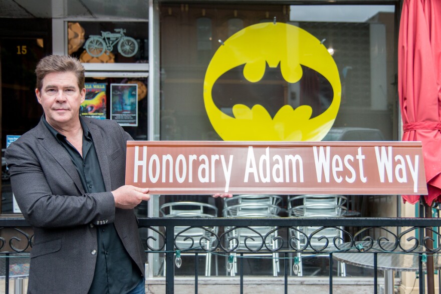 Actor who worked with Adam West holding a sign reading Honorary Adam West Way.