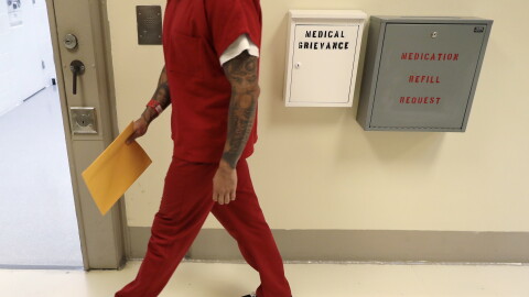 A person in an orange prison uniform walks down a hall. 