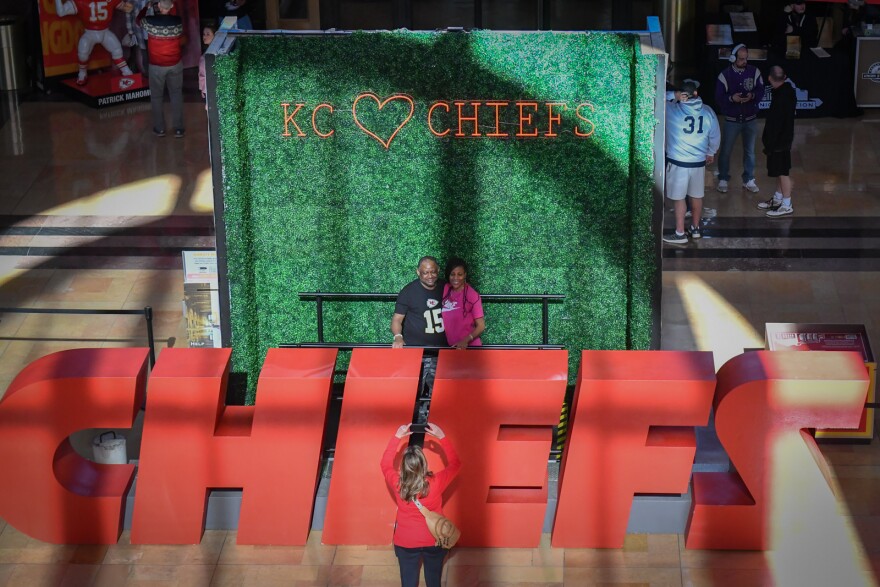 Photo looking from above inside a large room where light from a large window is falling on a display of life-sized letters that spell "CHIEFS." People are standing behind the letters while a person takes their photo.