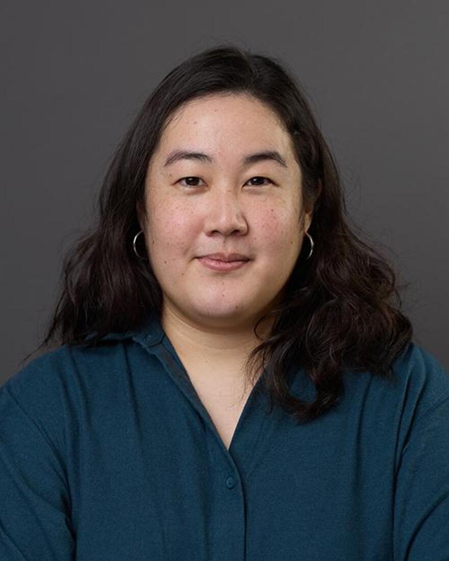 An Asian American woman, Sara Suzuki, is centered in a headshot, wearing a teal shirt and smiling