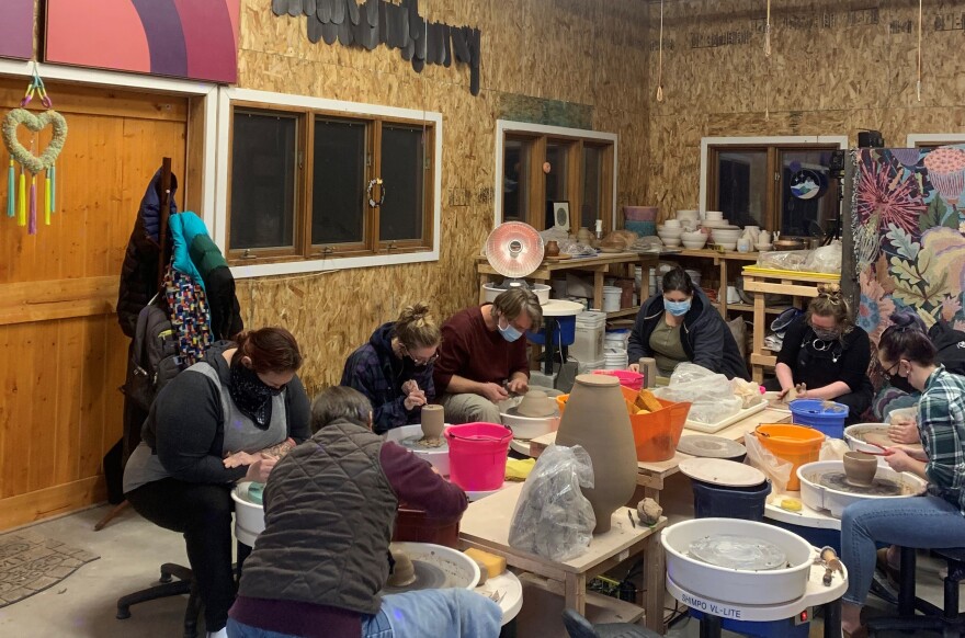 Seven students each sit at their own pottery wheel during a class in the expanded garage space used by Phi Pottery.