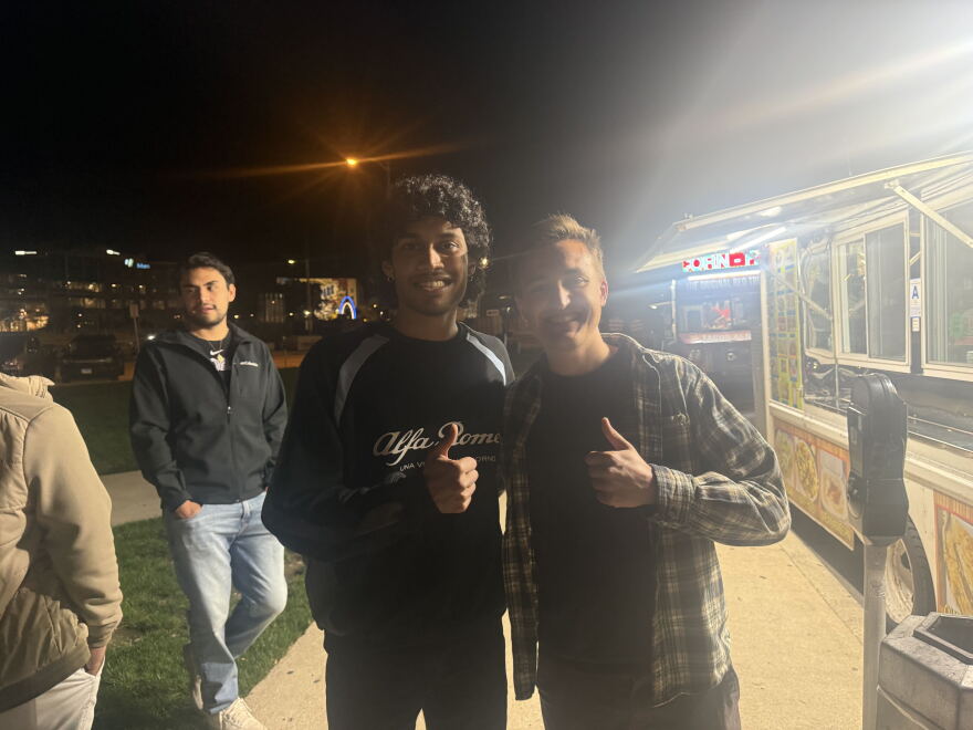 Two men standing, holding up a thumbs up, standing in front of a taco truck