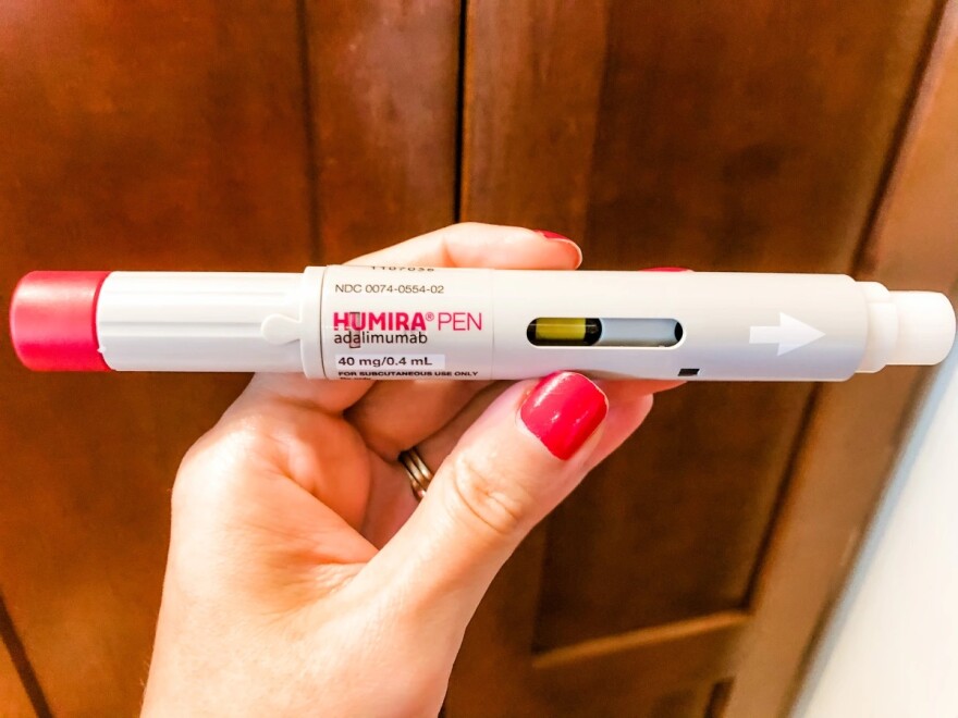 A person with pink fingernails holds an injectable Humira pen. 