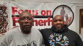 James Williams, left, and Keeyon Howard, right, smile at the camera and stand in front of a "Focus on Fatherhood" poster. 