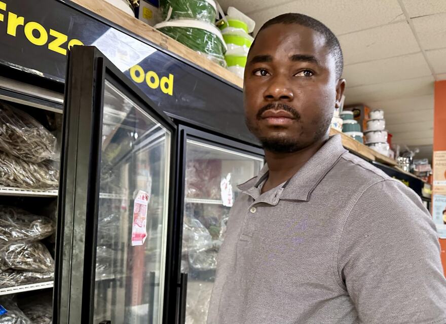 Black man stands next to a freezer with frozen fish imported from Tanzania 