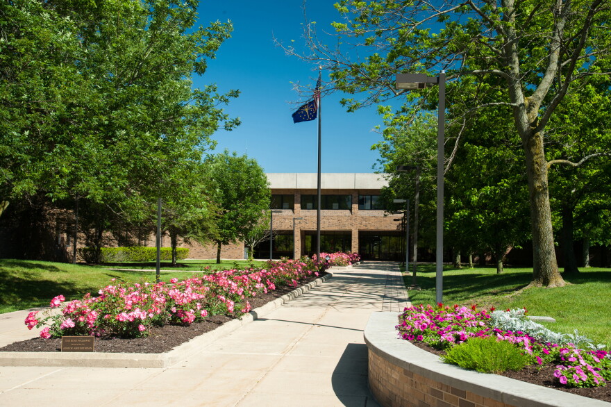 sidewalk leads up to a brown brick building. Flowers line the walkway.