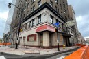 Orange barricades extend along the streets surrounding the Hotel Cadillac in downtown Rochester. A bent table frame is shown on the sidewalk. Some of the letters on the hotel sign are missing.